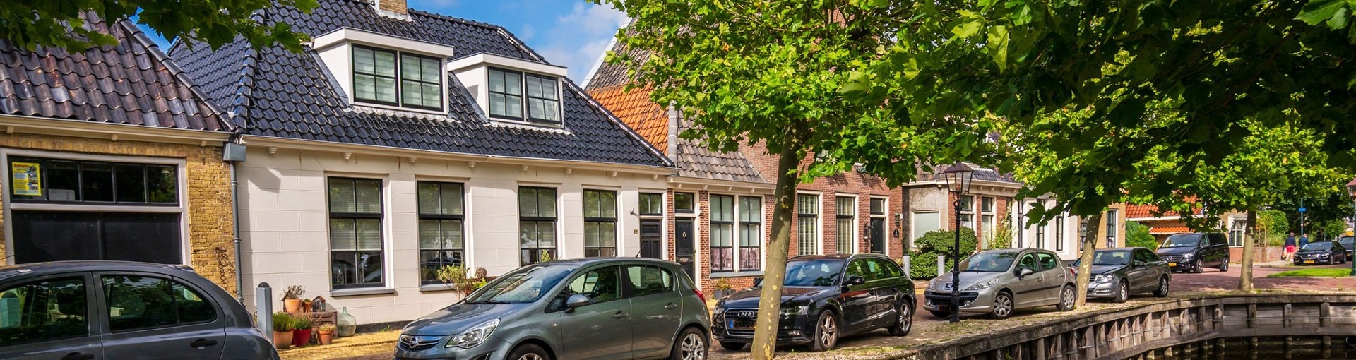 Een straat in Harlingen met huizen en auto's en een bootje in de gracht